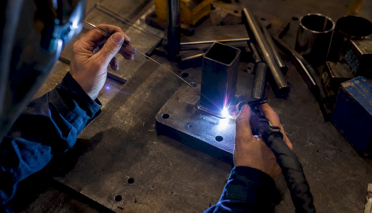 Hands feeding filler rod during TIG welding
