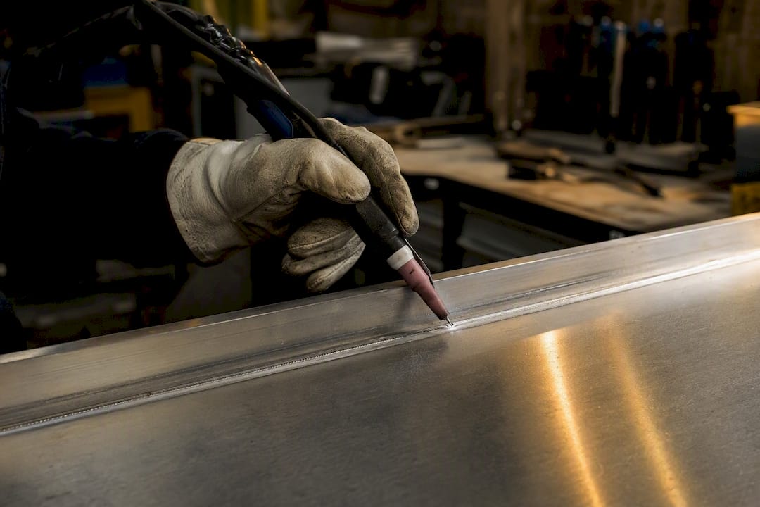Main du soudeur guidant la torche TIG sur de l'aluminium