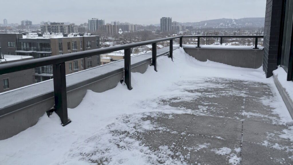 Uneven snow drift beside rooftop terrace railing