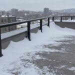 Uneven snow drift beside rooftop terrace railing
