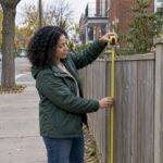 Homeowner measuring a fence at a Montreal corner lot