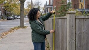 Homeowner measuring a fence at a Montreal corner lot
